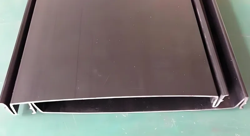 Primer plano de un perfil o extrusión metálica plana de color negro colocada sobre una superficie verde.