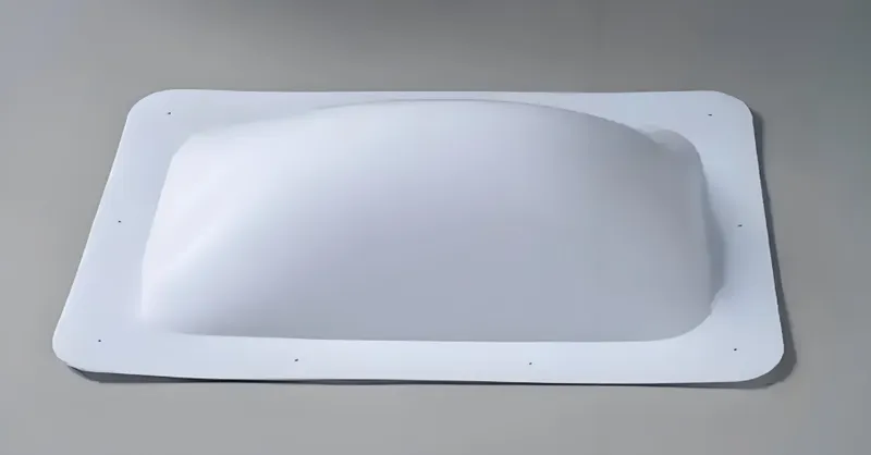 A rectangular white plastic skylight with a curved shape and small holes along the edges, placed on a flat surface