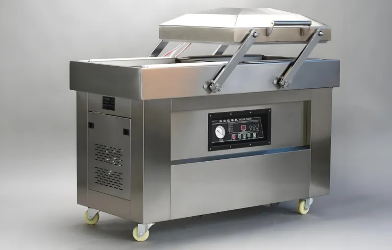 A large industrial vacuum sealing machine with a metal body and control panel, equipped with wheels for mobility