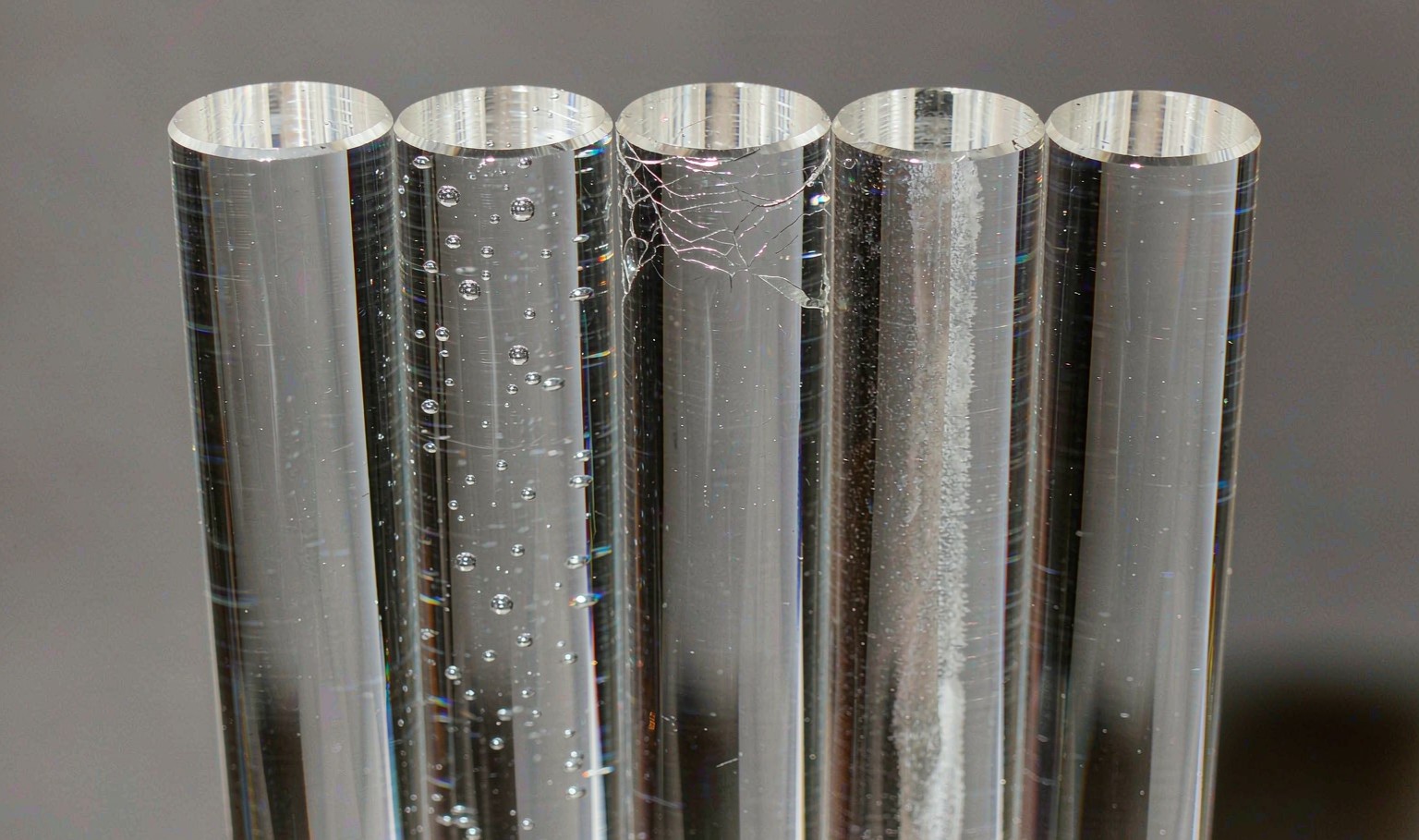 Close-up of acrylic rod ends showing bubbles, crazing and a milky colour streak beside a clear rod
