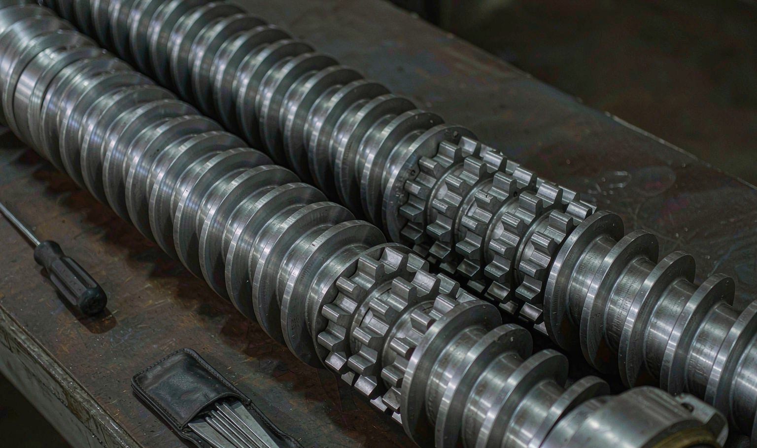 Two intermeshing parallel twin extruder screws with kneading block elements on a workshop bench