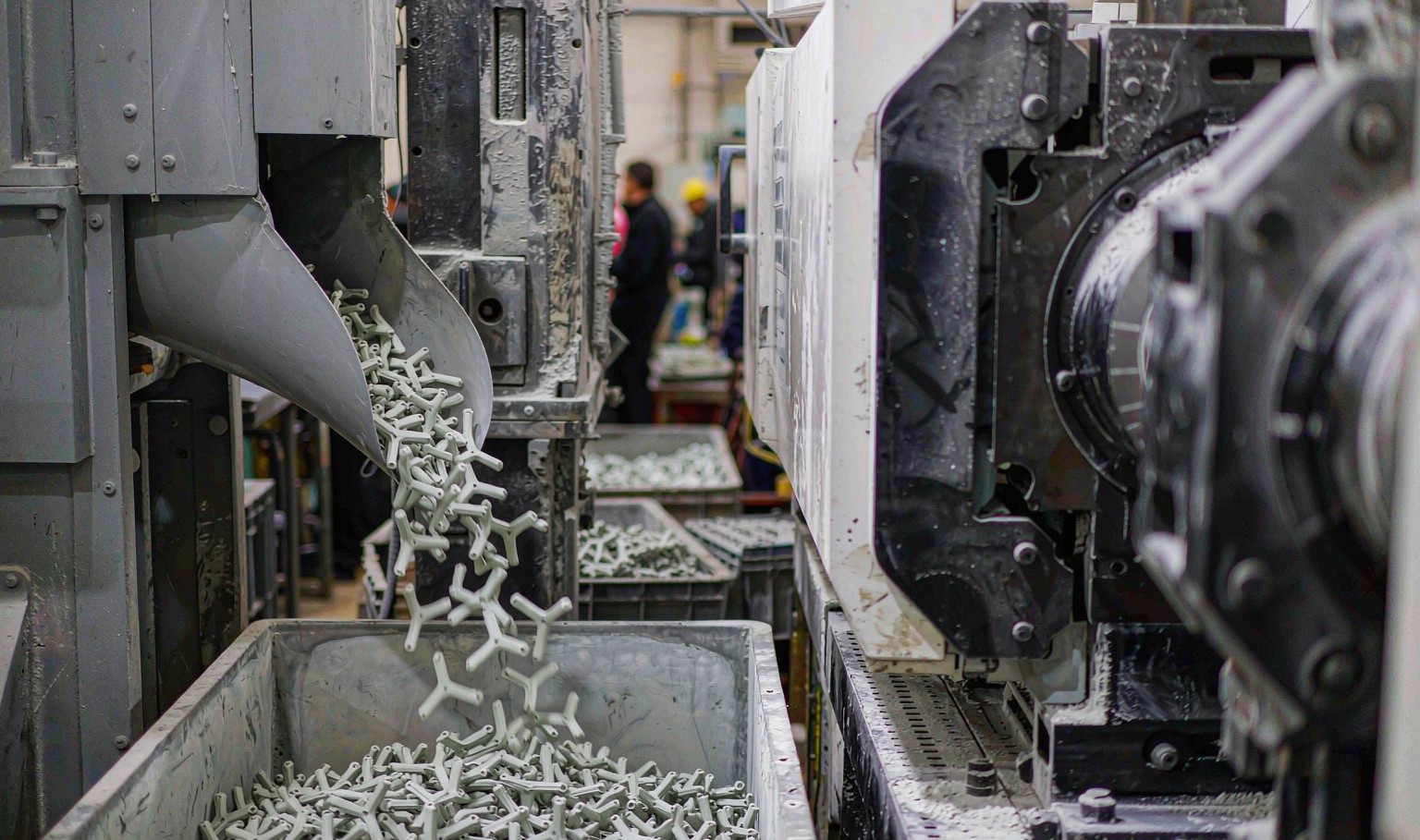 Freshly moulded plastic components dropping into a collection bin beside an injection moulding machine
